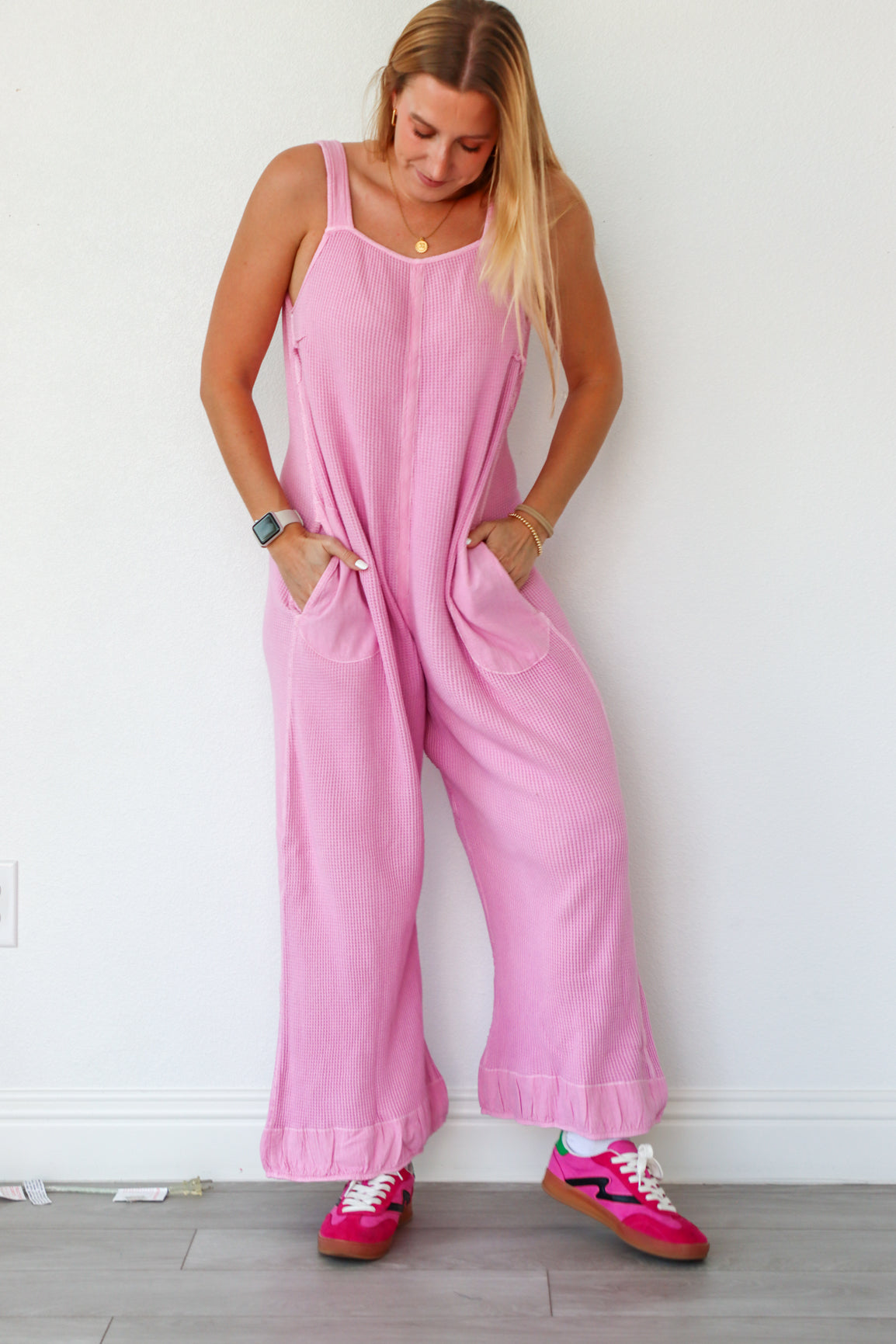 Woman wearing a pink jumpsuit against a white wall