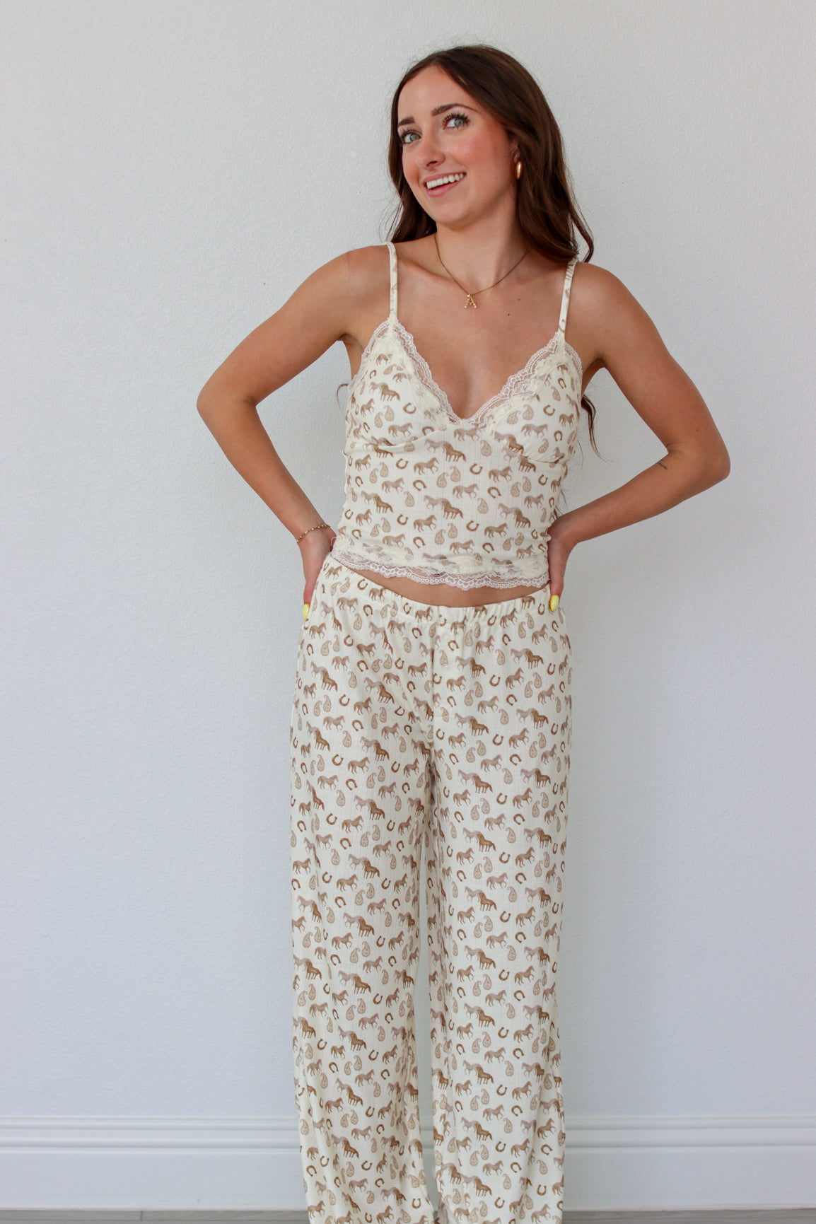 Woman wearing a cream lace top with western motifs with matching pants against a light background