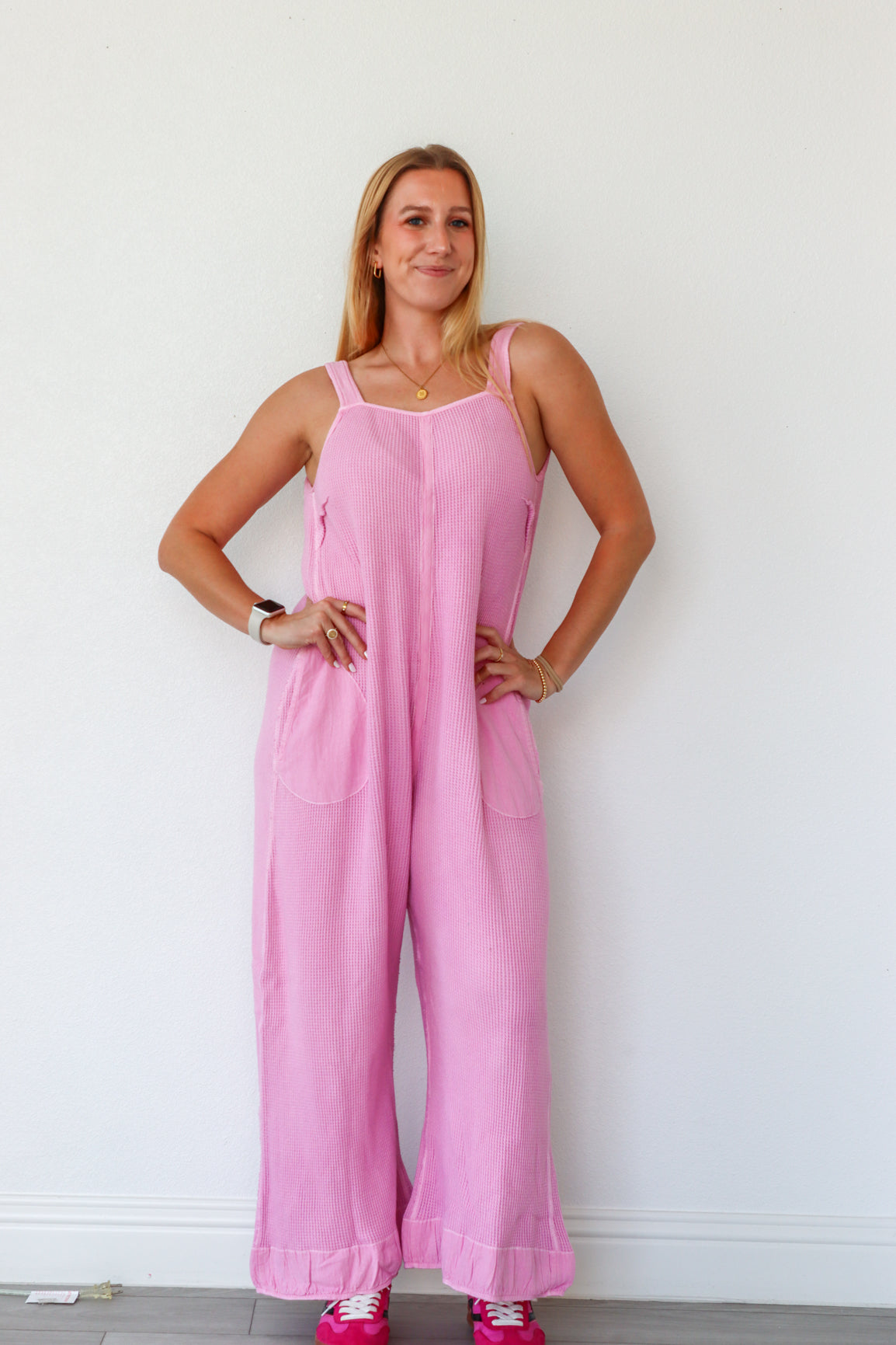 Woman wearing a pink jumpsuit against a white wall