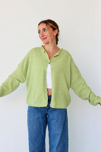 Person wearing a light green cardigan and blue jeans against a white background