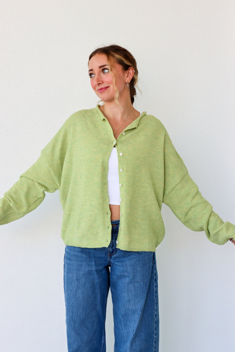 Person wearing a light green cardigan and blue jeans against a white background