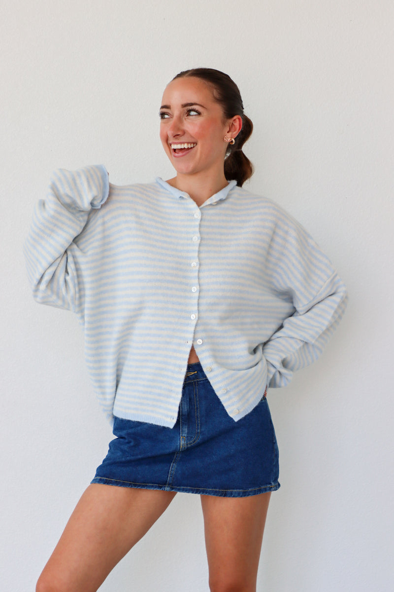 Woman wearing a light blue striped sweater and denim skirt against a white background