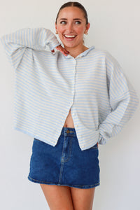 Woman wearing a light blue striped shirt and denim skirt on a white background