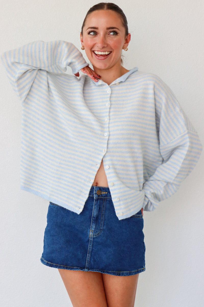 Woman wearing a light blue striped shirt and denim skirt on a white background