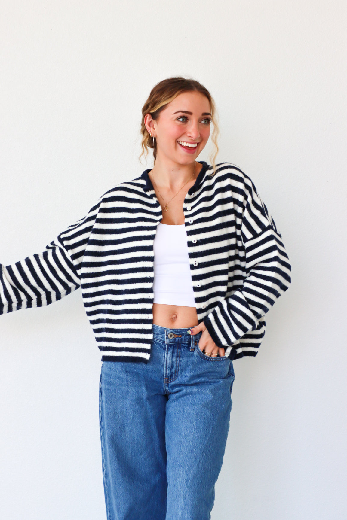 Woman wearing a black and white striped cardigan, white top, and blue jeans against a white background