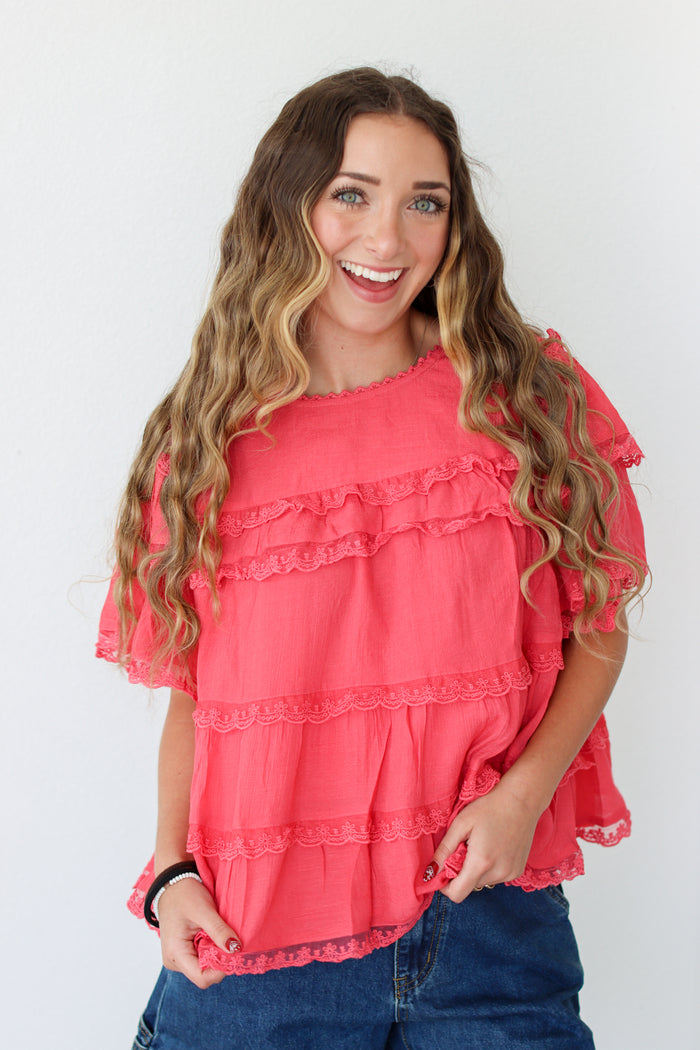 Woman wearing a coral ruffled top against a white background