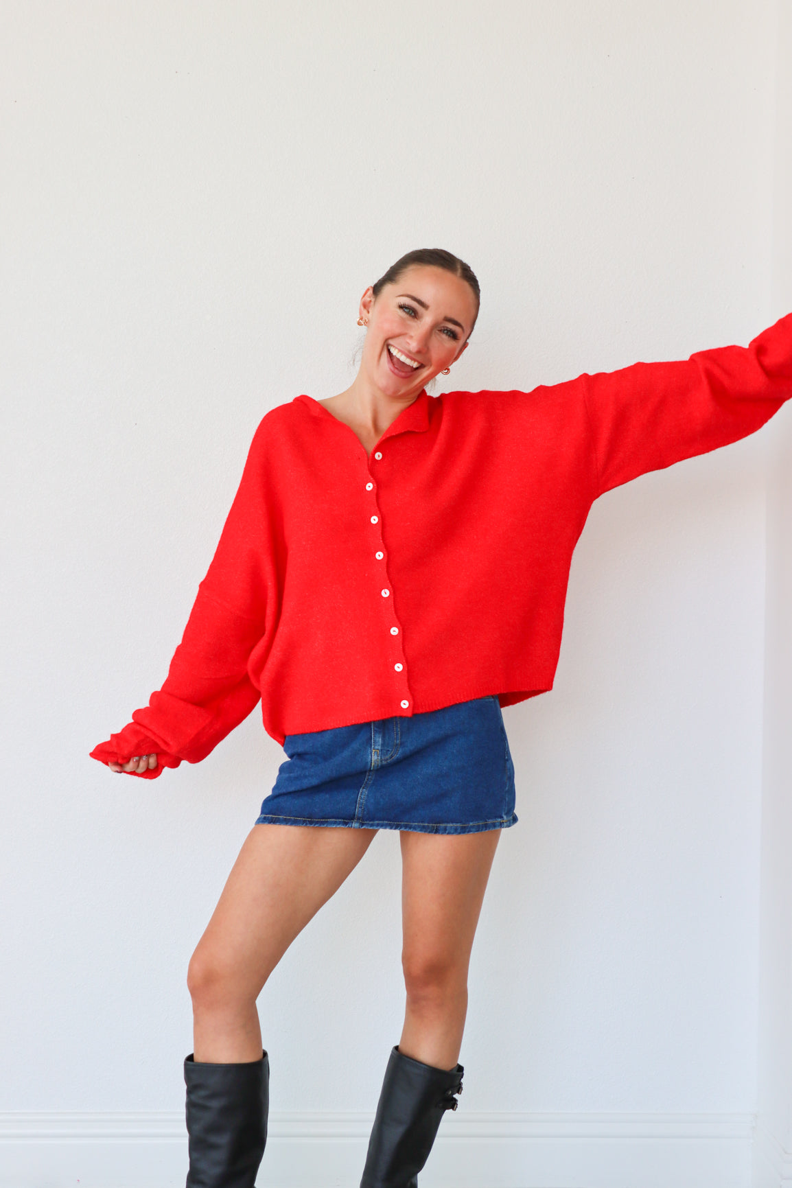 Person wearing a red sweater and blue skirt with black boots against a white background