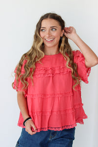 Woman wearing a coral ruffled top against a white background