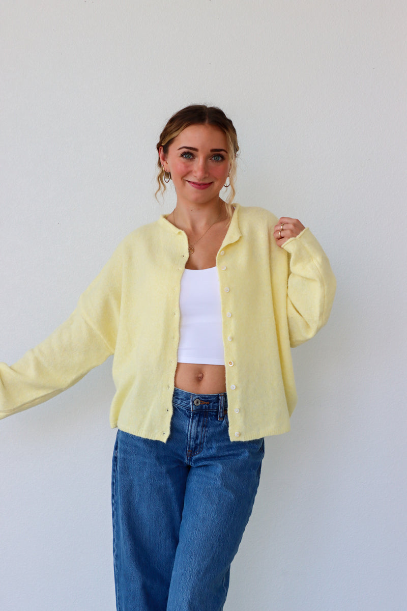 Person wearing a light yellow jacket over a white top and blue jeans against a plain background