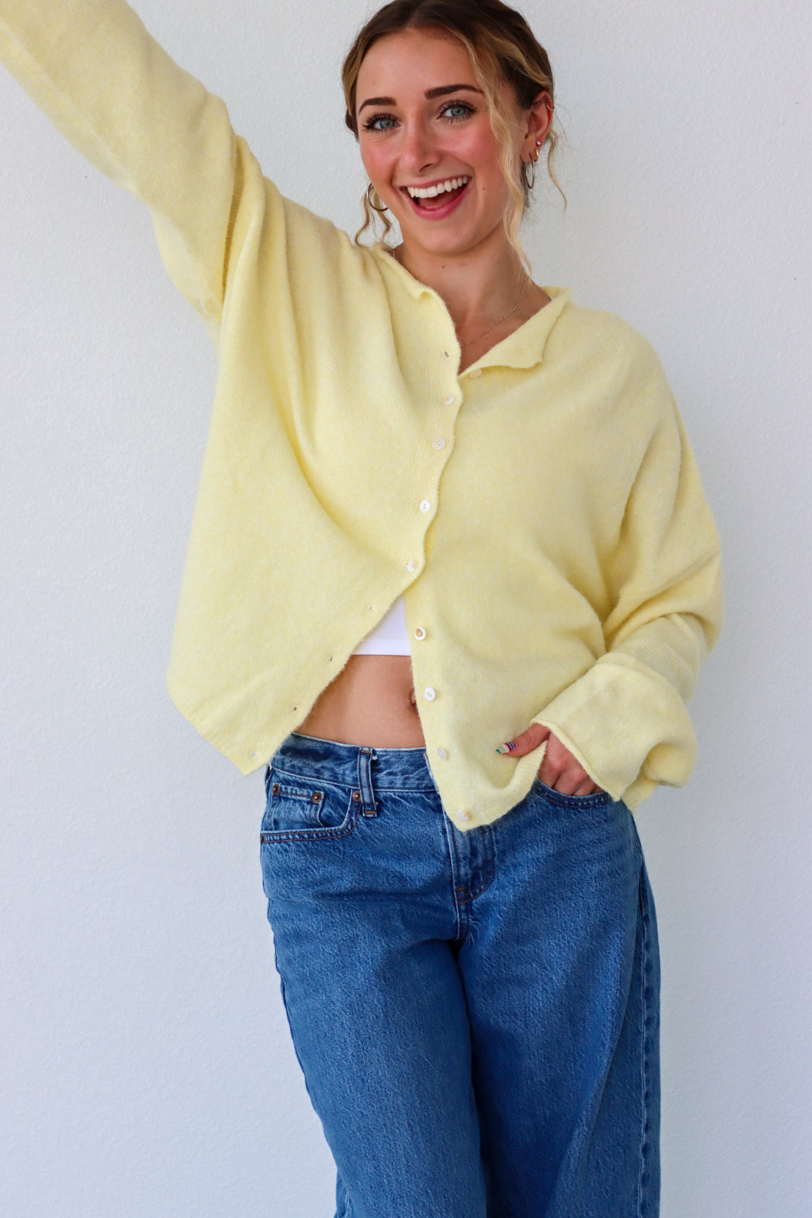 Person wearing a light yellow cardigan and blue jeans against a white background