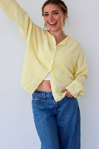 Person wearing a light yellow cardigan and blue jeans against a white background