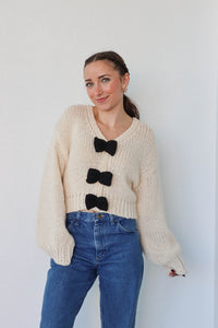 girl wearing cream knit sweater with black bow detailing