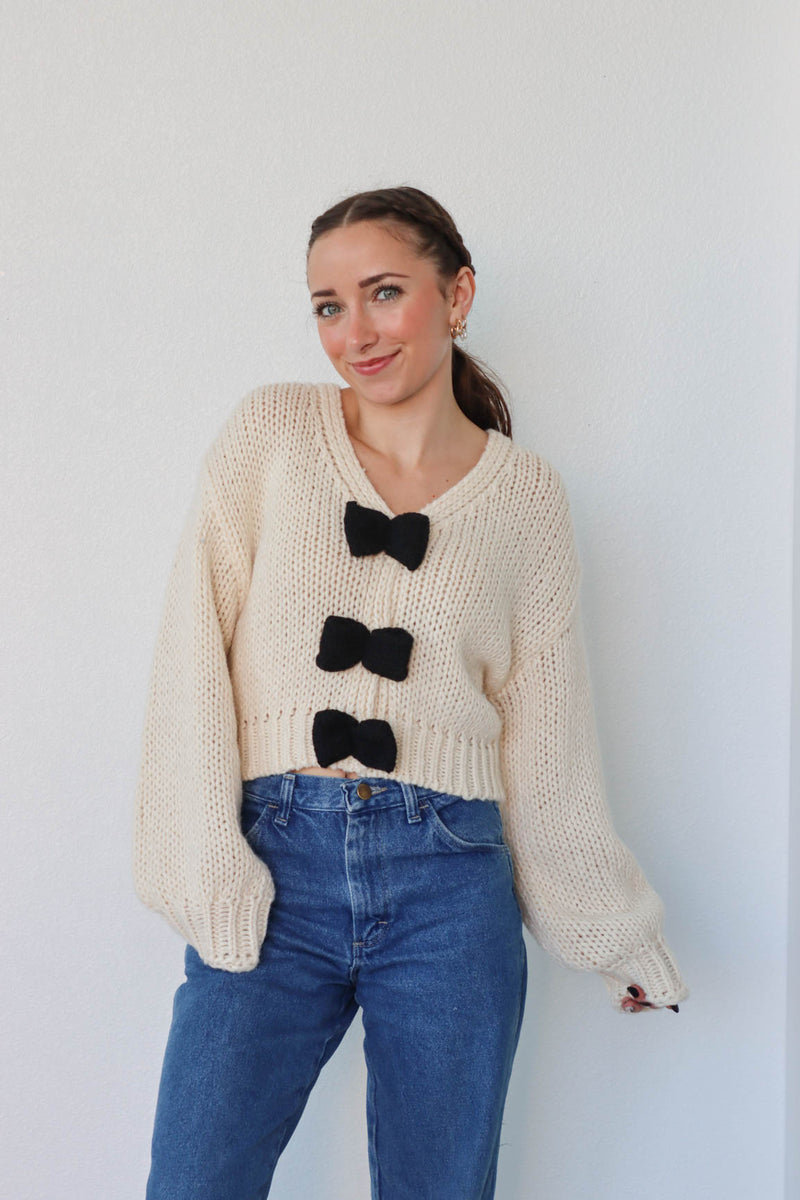 girl wearing cream knit sweater with black bow detailing