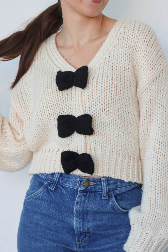 girl wearing cream knit sweater with black bow detailing