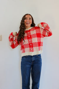 Person wearing a red and white checkered shirt with a white top underneath, standing against a plain background.