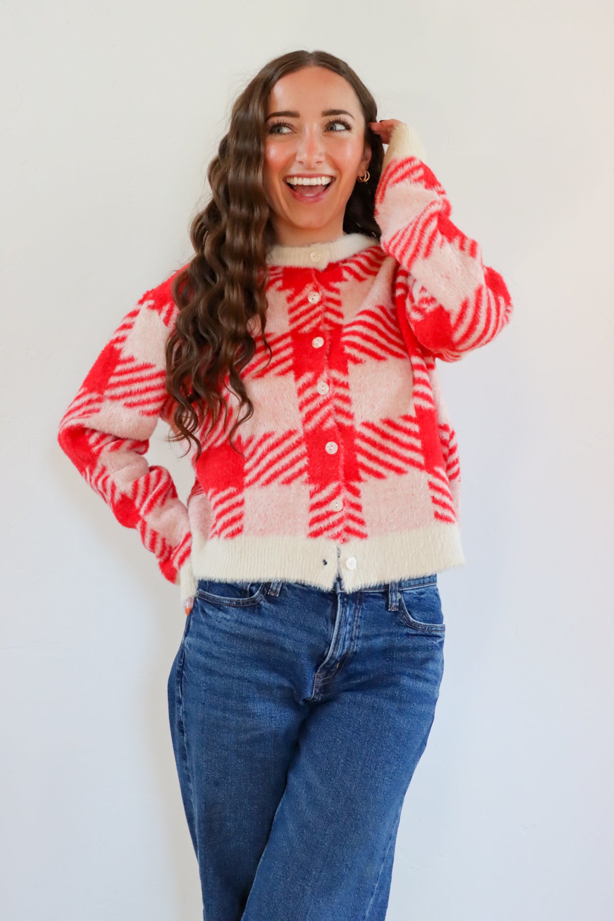 Woman wearing a red and white checkered sweater with blue jeans against a plain background