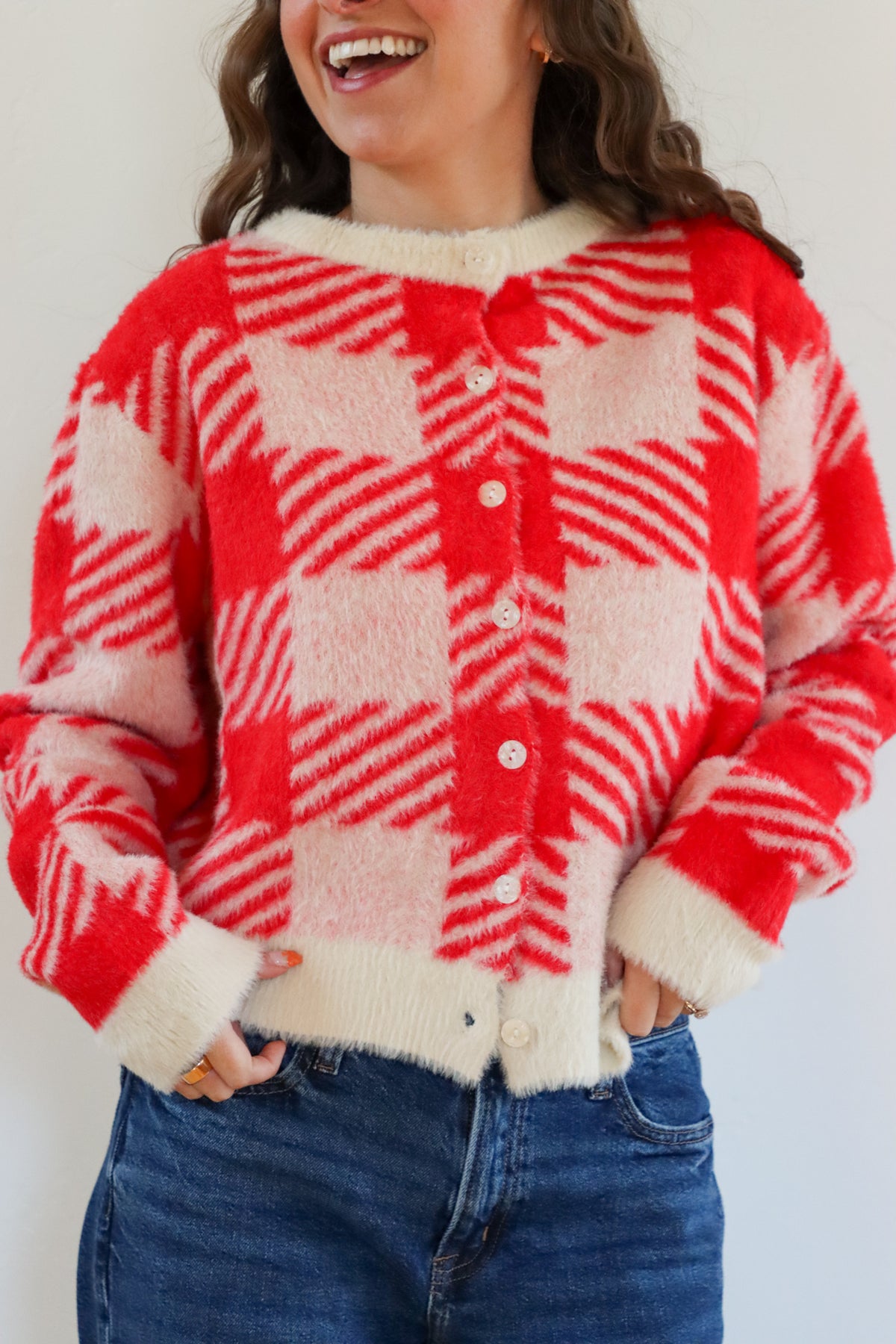 Person wearing a red and white checkered cardigan with a plain background