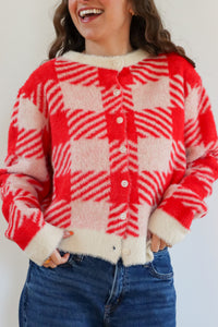 Person wearing a red and white checkered cardigan with a plain background