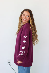 Woman wearing a purple crewneck with a embroidery design against a white background 