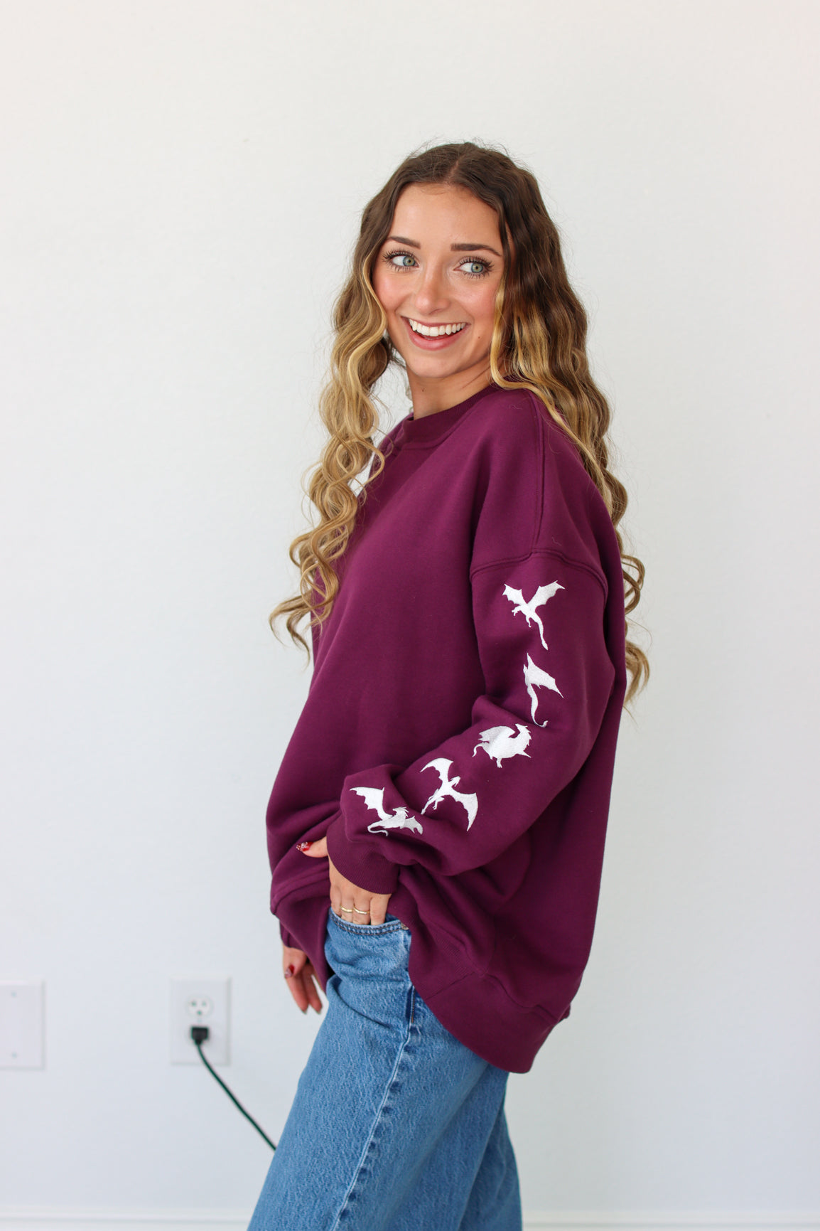 Woman wearing a purple crewneck with a embroidery design against a white background 