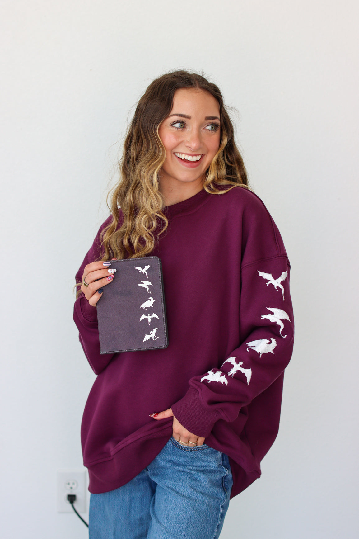 Woman wearing a purple crewneck with a embroidery design against a white background 