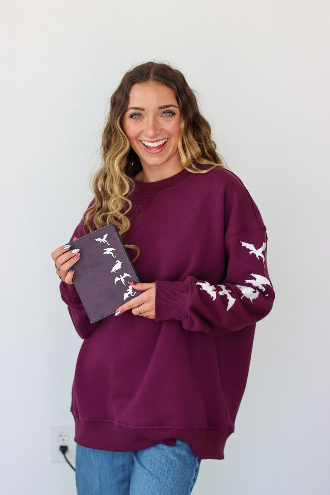 Woman wearing a purple crewneck with a embroidery design against a white background 