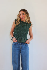 Woman wearing a green top and blue jeans against a white background