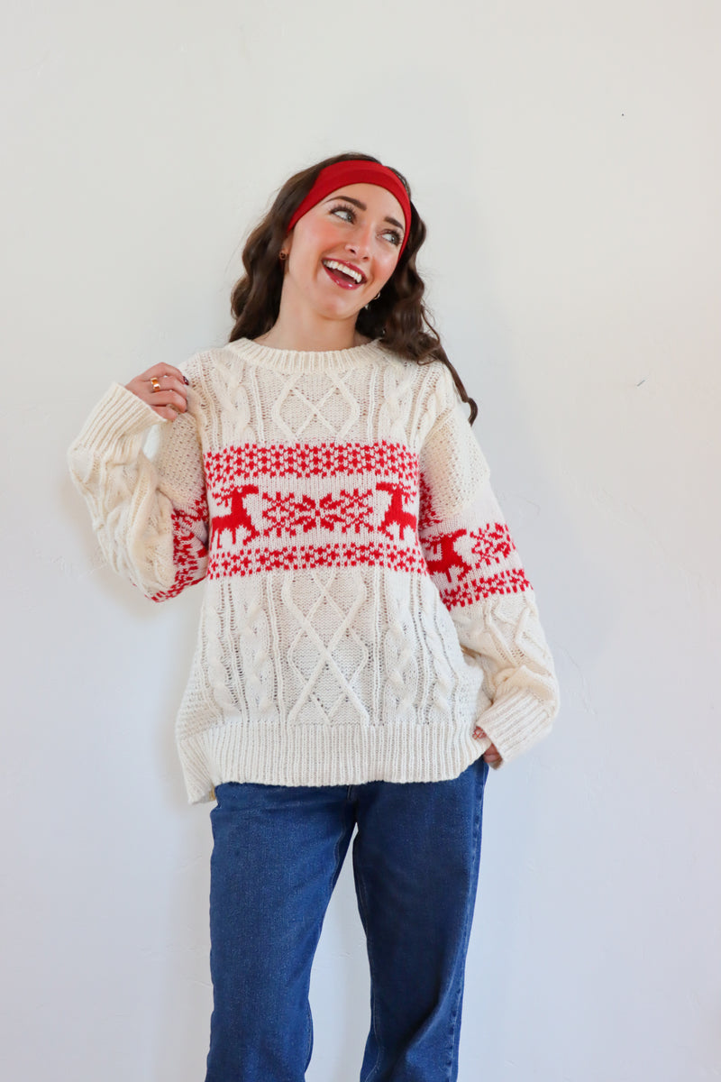 Woman wearing a cream sweater with red reindeer pattern against a white background