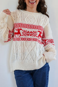 Person wearing a cream sweater with red deer pattern against a white background