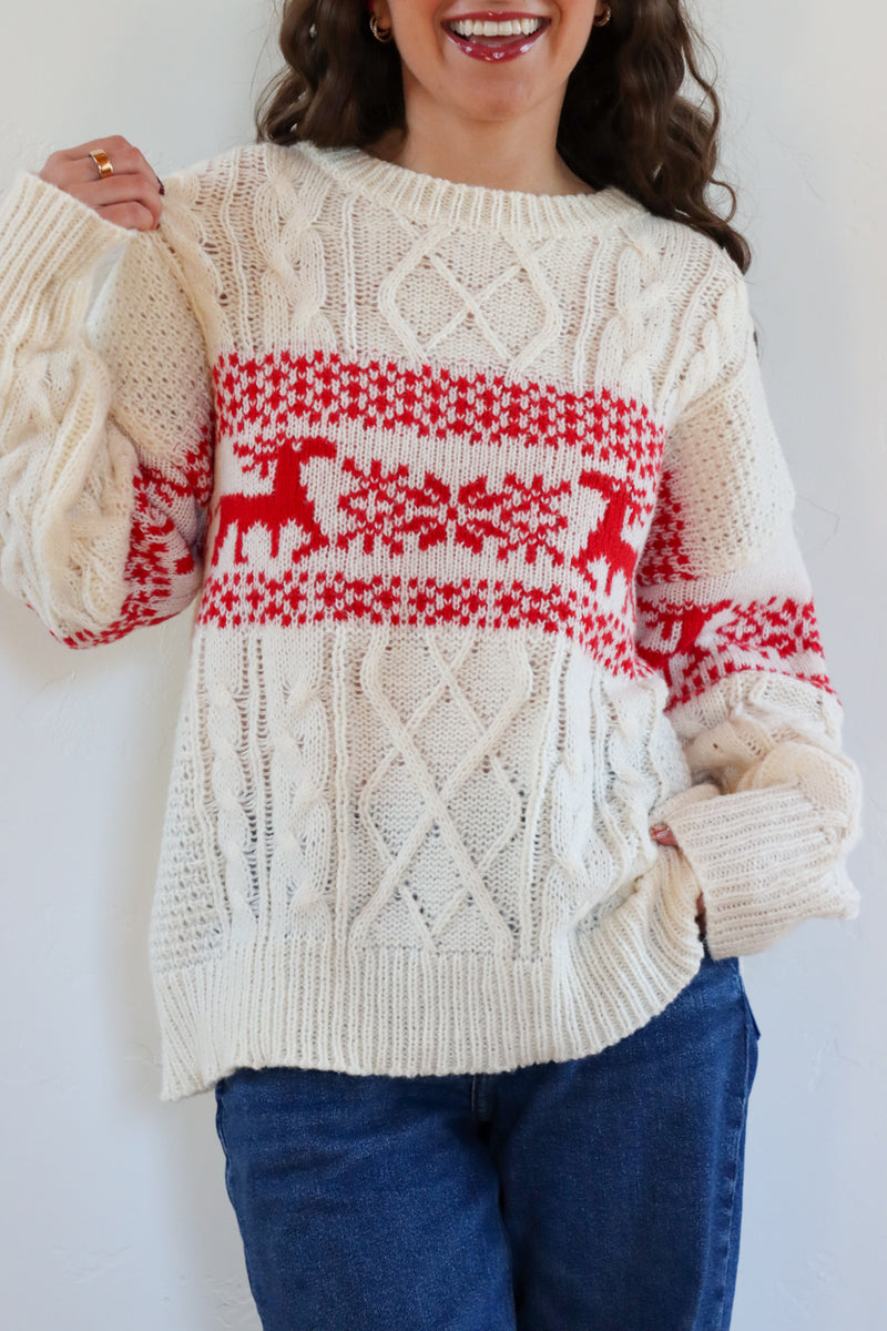 Person wearing a cream sweater with red deer pattern against a white background