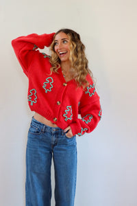 Woman wearing a red cardigan with green patterns and blue jeans against a white background