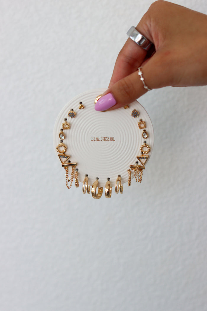 Hand holding a round white jewelry holder with gold earrings on a light gray background