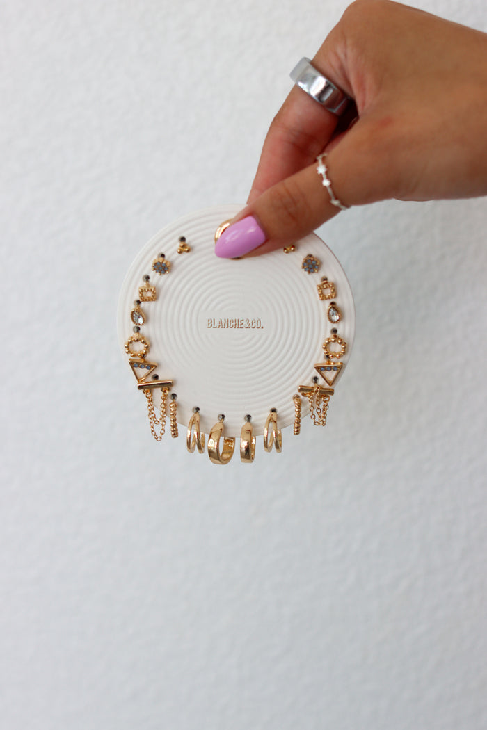 Hand holding a white jewelry display tray with gold earrings on a light gray background