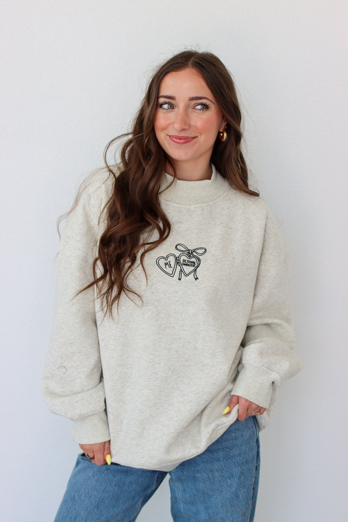 Woman wearing a light gray crewneck with a embroidery design against a white background 