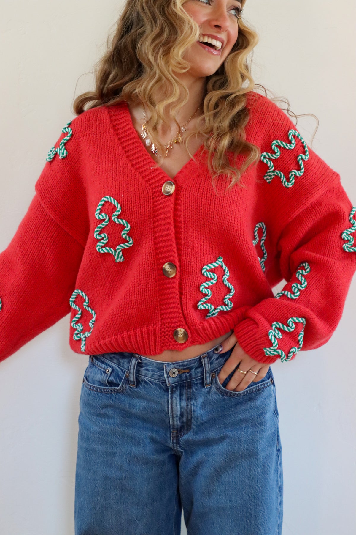 Person wearing a red cardigan with green patterns and blue jeans against a white background