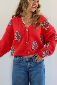 Person wearing a red cardigan with green patterns and blue jeans against a white background