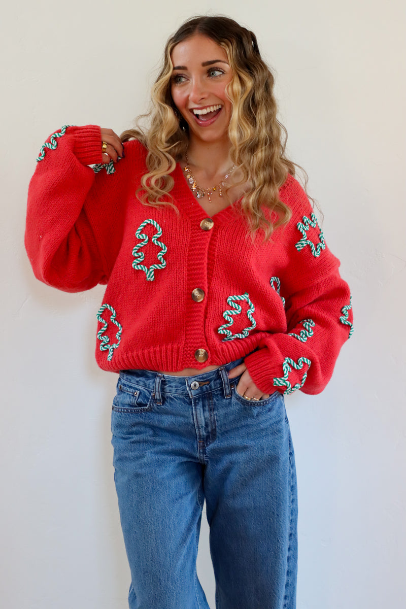 Woman wearing a red sweater with green patterns and blue jeans against a white background