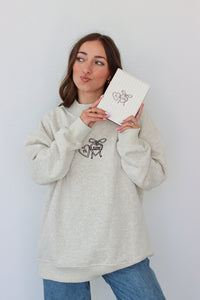 Woman wearing a light gray crewneck with a embroidery design against a white background 
