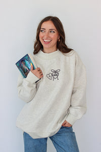 Woman wearing a light gray crewneck with a embroidery design against a white background 