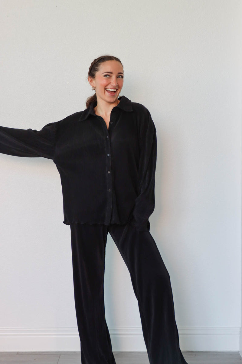 girl wearing black outfit set with long sleeve button down blouse and elastic waist palazzo pants. Both in a pleated crinkle fabric