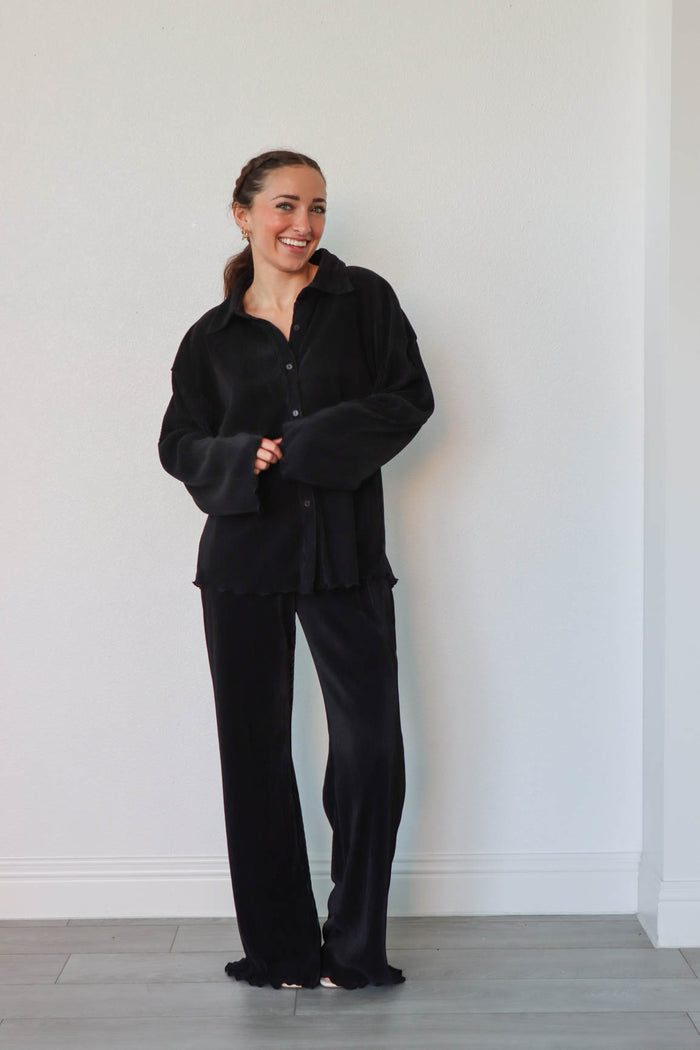 girl wearing black outfit set with long sleeve button down blouse and elastic waist palazzo pants. Both in a pleated crinkle fabric