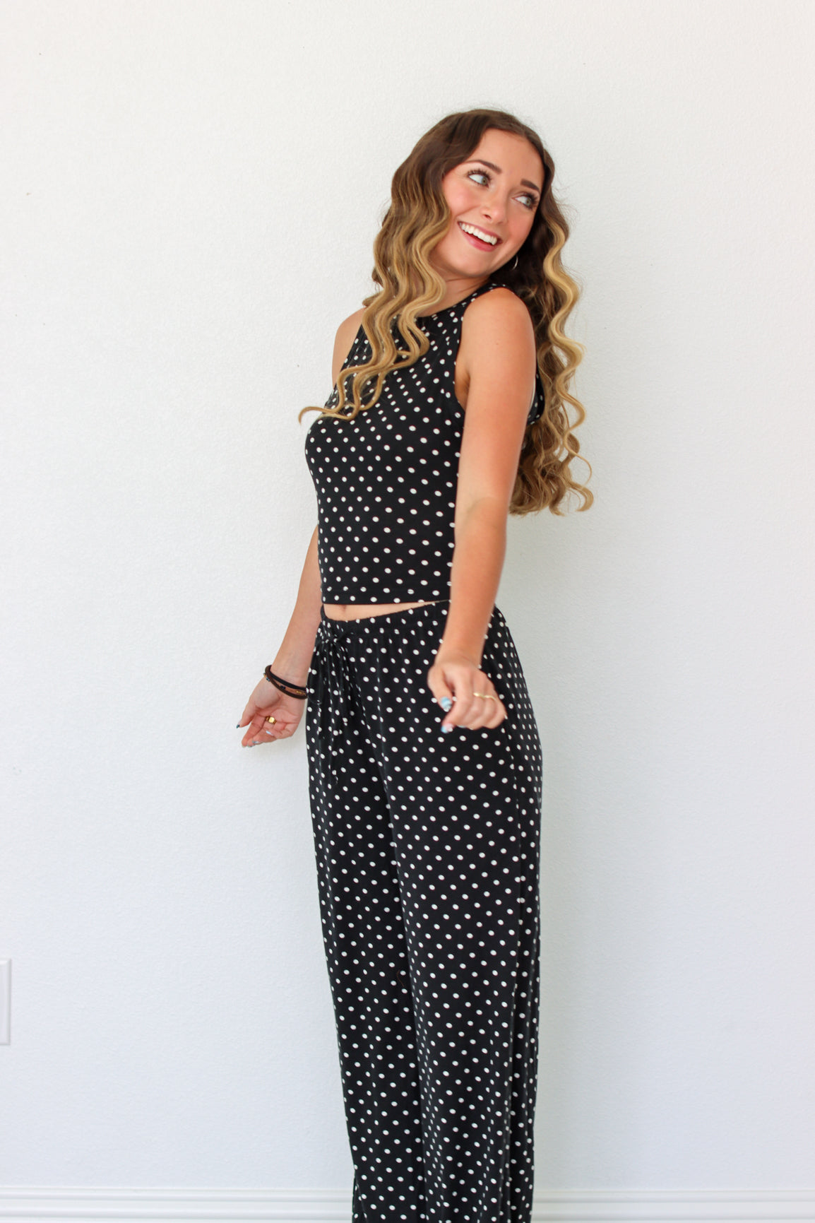A woman modeling a black sleeveless set with white polka dots, standing against a plain white wall.