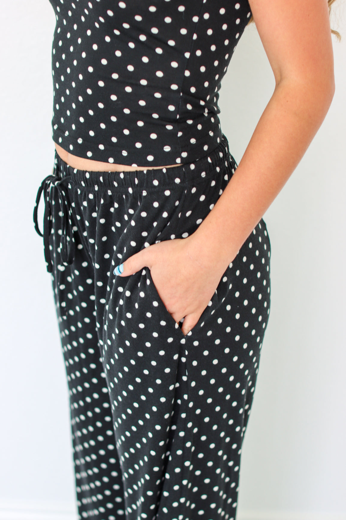 A person wearing a black two-piece set with white polka dots, featuring a sleeveless crop top and matching drawstring pants with side pockets.