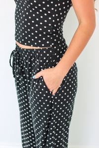 A person wearing a black two-piece set with white polka dots, featuring a sleeveless crop top and matching drawstring pants with side pockets.
