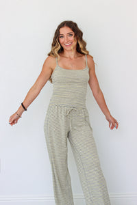 A woman modeling a light sage green and yellow striped camisole set with a drawstring waist, standing against a plain white wall.