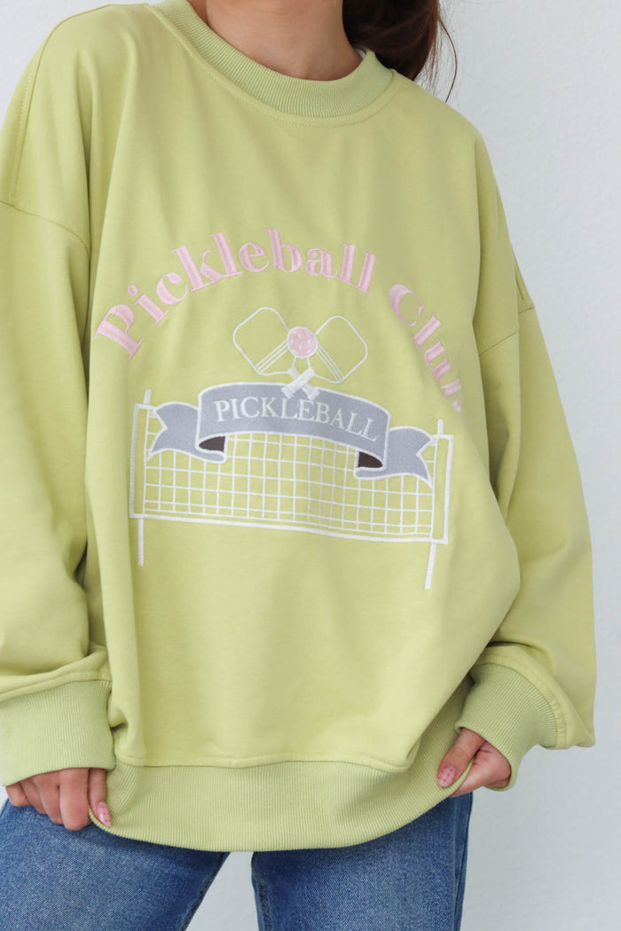 girl wearing lime green crewneck sweatshirt with embroidered pickle ball graphic