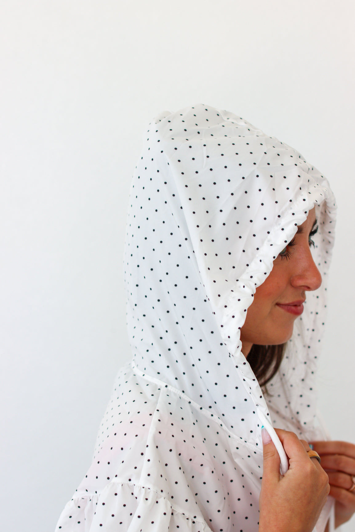 A woman wearing a white hood with small black polka dots, shown in profile against a plain white background.