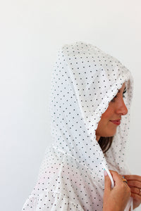 A woman wearing a white hood with small black polka dots, shown in profile against a plain white background.