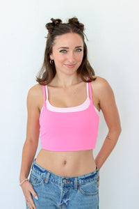 A woman modeling a bright pink crop top with a contrasting light pink scoop neckline, paired with blue jeans, against a plain white background.