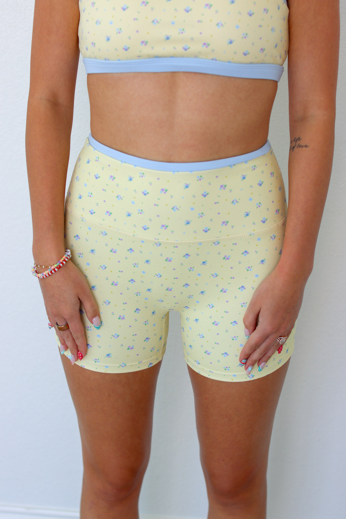 A model wearing a matching two-piece activewear set featuring a pale yellow and light blue micro-patterned crop top and high-waisted shorts.